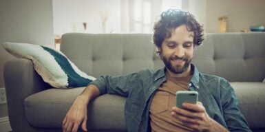 Man sits on the sofa with cell phone and informs himself about eharmony settings