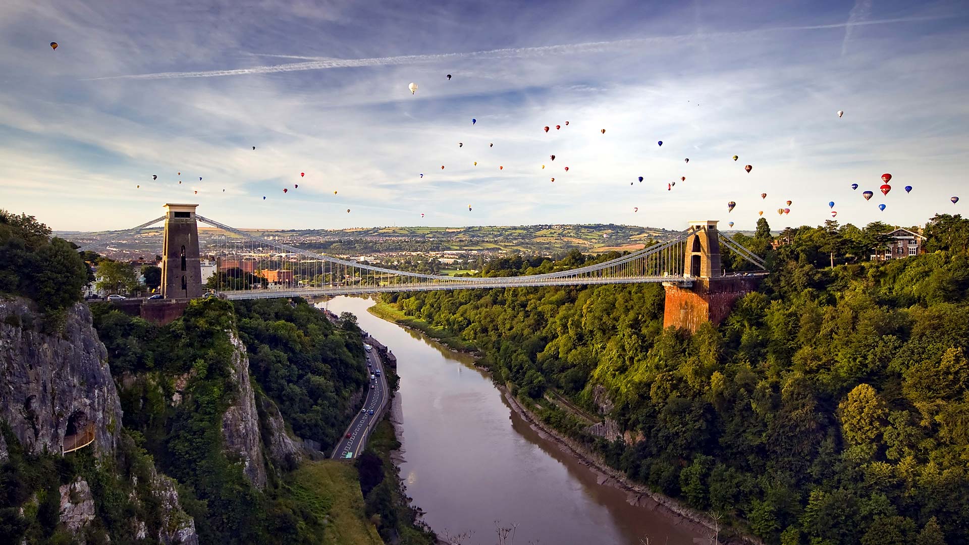Clifton Suspension Bridge overlooking the Avon Gorge with hot air balloons in the sky.