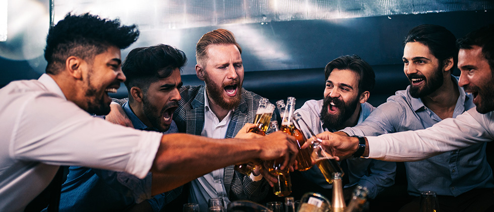 A group of young men bring their beer bottles together in a toast