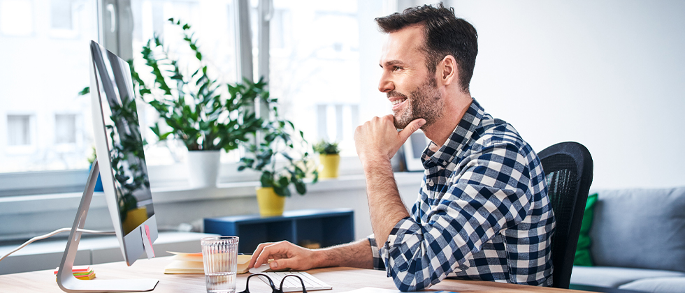 A man sits at his desk, looking at his monitor