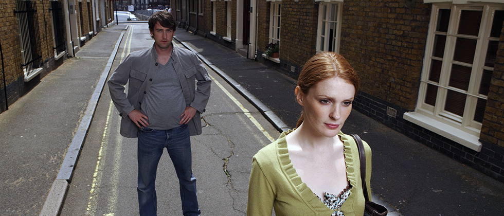 A red-haired woman walks away from a man on a narrow strees