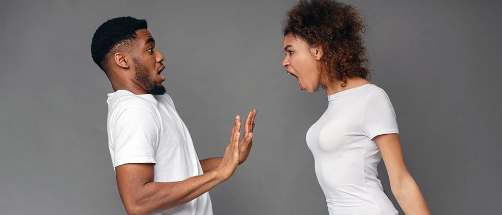 A woman yells angrily in the face of a man, who backs away in surprise