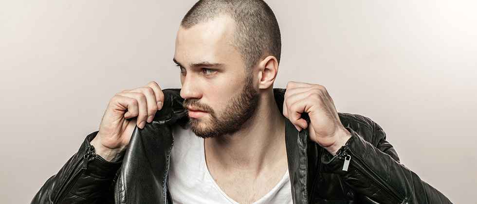 A young, shaven-headed man pulls the collar up on a black leather jacket
