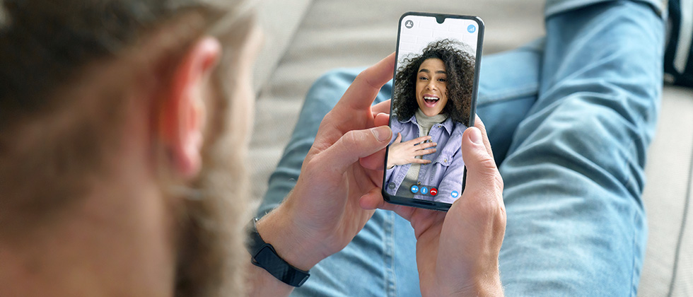 A man sits on a sofa holding a phone, talking to his date on screen