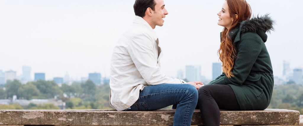 Man and woman sitting on bench looking at each other as symbol for first date tips