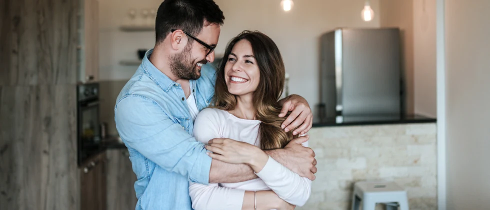 Couplein their kitchen hugging while smiling at each other 