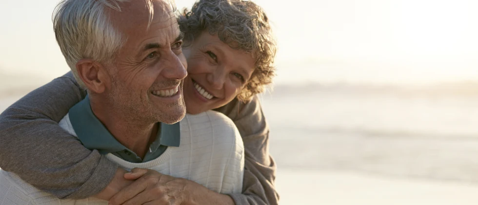 A man and a woman hug each other at the beach and both are smiling.