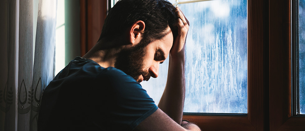 A man leans on a windowsill, head in hands