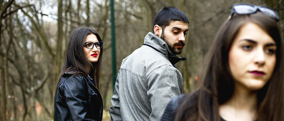 A man walks with his girlfriend while looking back at another woman