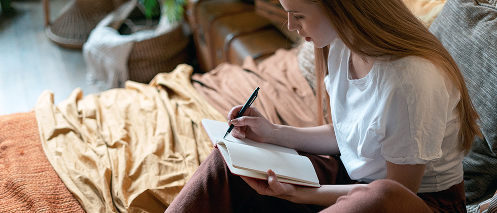 A young woman sits on her bed writing in a notebook
