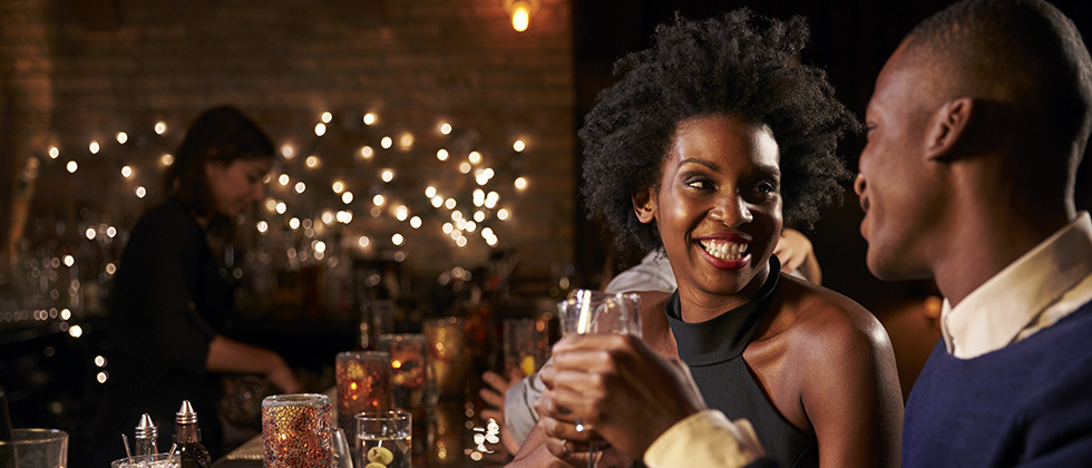 A couple touch glasses while enjoying a drink at a cocktail bar