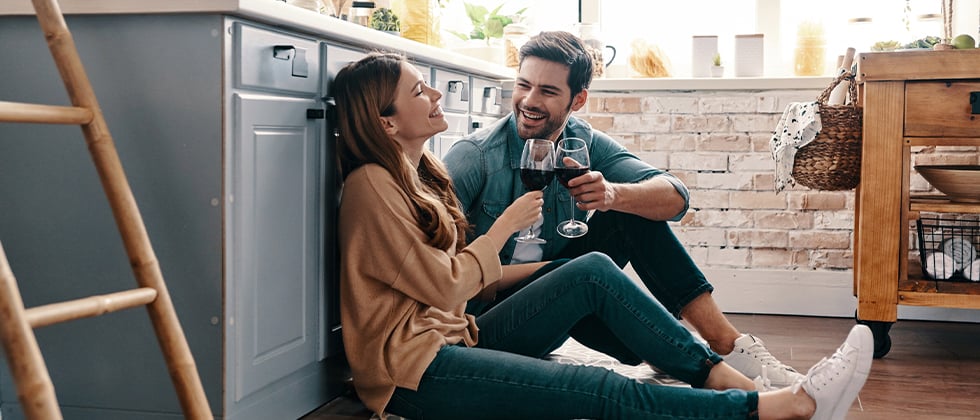 A coupld drinking wine while sitting on the floor of their kitchen