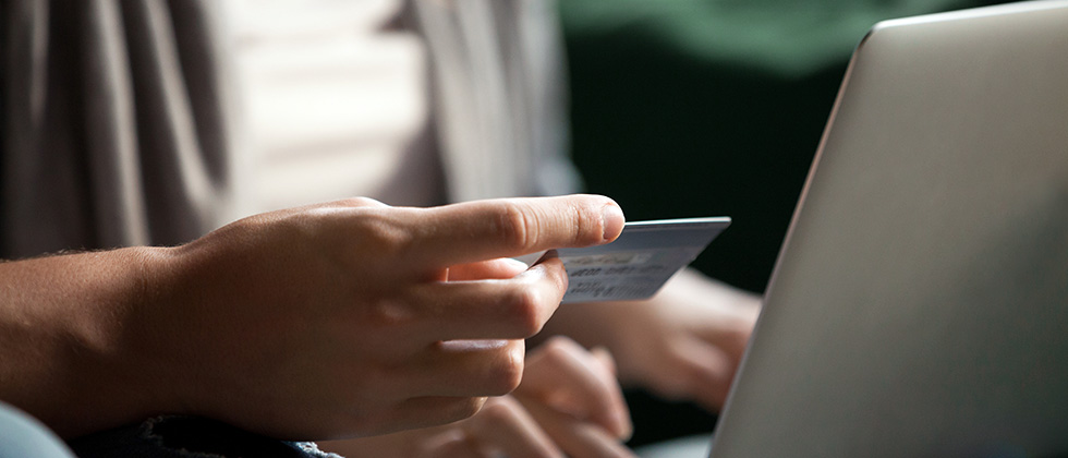 Close-up of a man's hands holding a credit card in front of a laptop