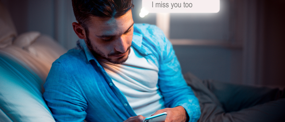 A man in bed texting 'I miss you too' on his phone