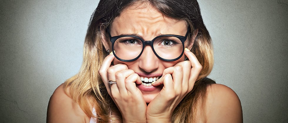 A nervous woman looks to camera, biting her nails