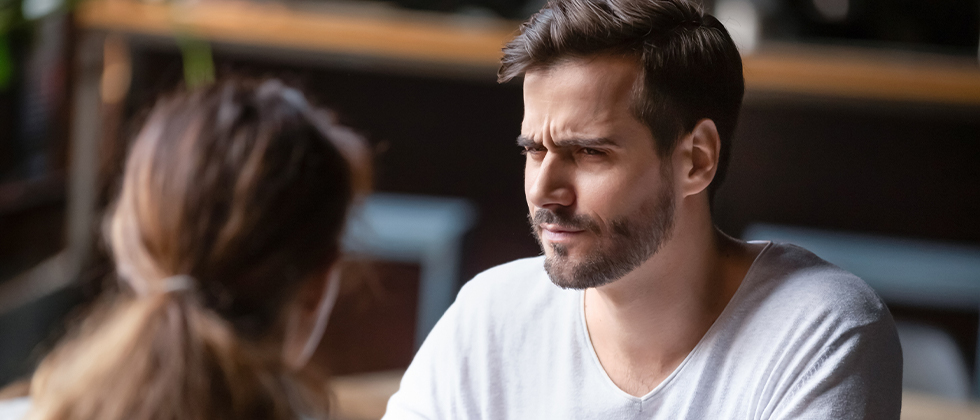 A man looks across the table at his date, a quizzical look on his face