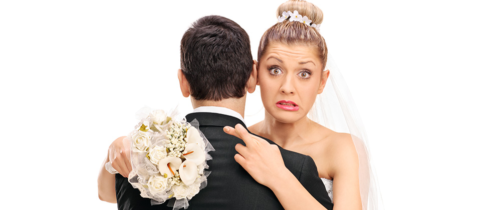 A bride hugs her new husband with fingers crosssed behind his back