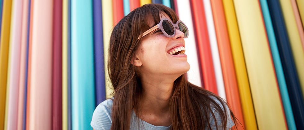 A woman in sunglasses in front of a colourful, striped background