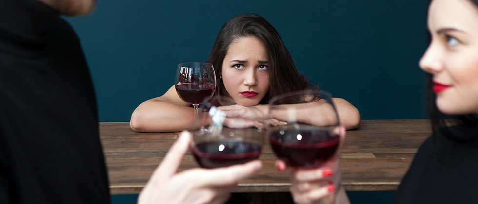 A woman in a wine bar looks troubled as she looks at two of her friends talking