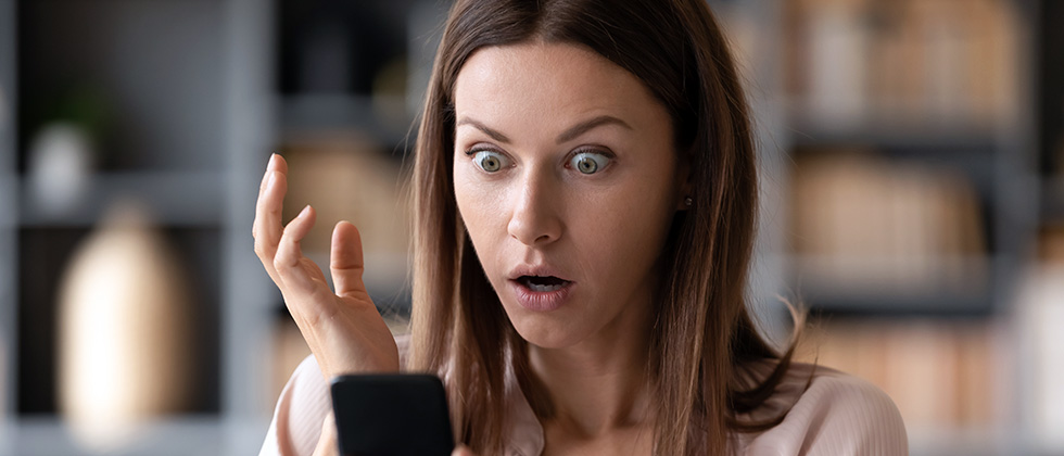A young woman looks at her phone with an expression of shock on her face