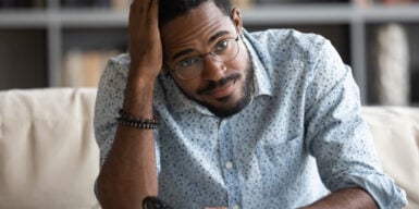 A guy in glasses sitting looking confused with her hand on his head