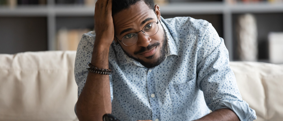 A guy in glasses sitting looking confused with her hand on his head