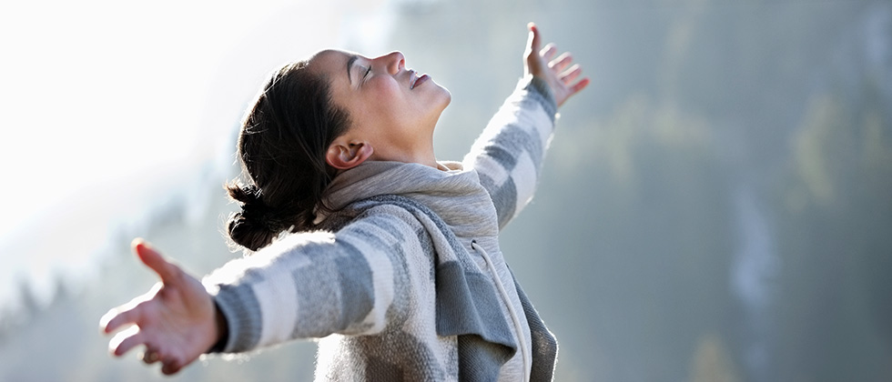 A woman stands with open arms, her face raised to the sky