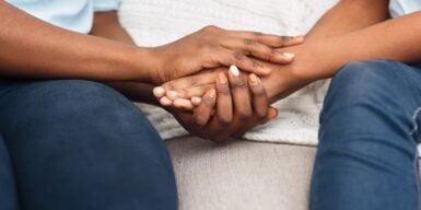 A couple holding hands on the couch in a comforting way