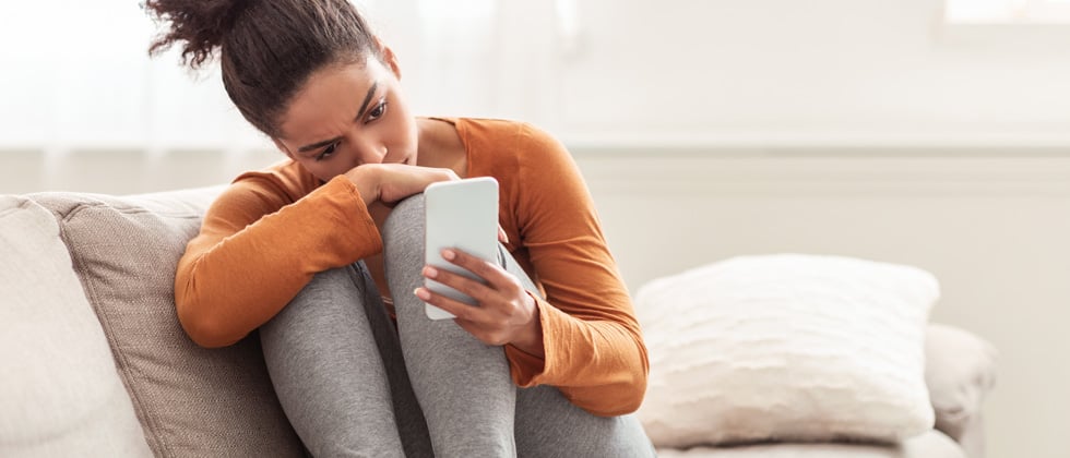 A woman curled up on the couch looking into her phone concerned