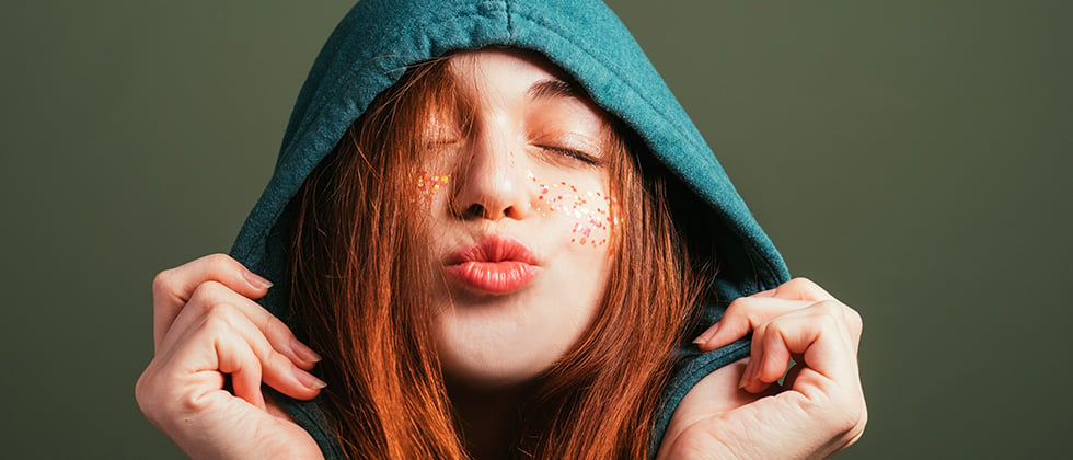 A red-haired young woman in a hood purses her lips