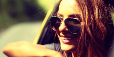 A woman in a car with sunglasses smiling while her head is out the window