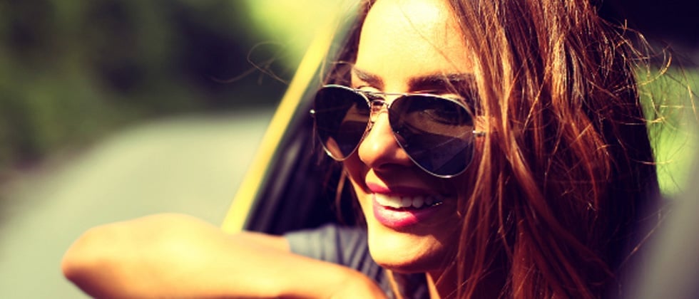 A woman in a car with sunglasses smiling while her head is out the window