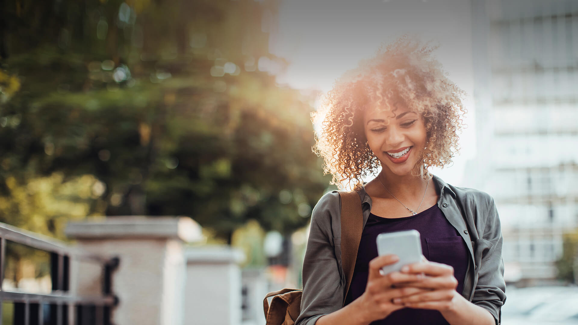 Black single woman smiles in her smartphone while dating online on the go in UK