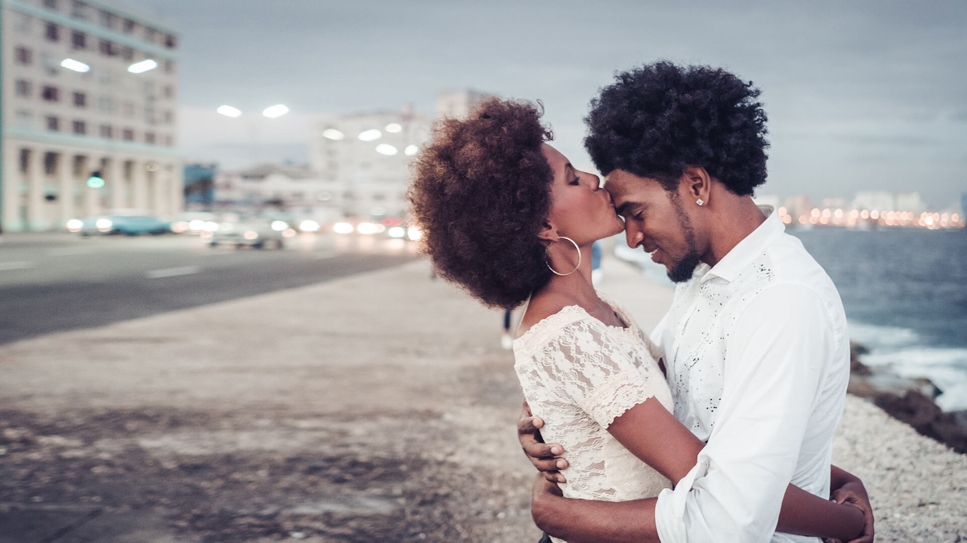 carribean dating symbolized by a woman who embraces a man and gives him a kiss on the forehead at the beach