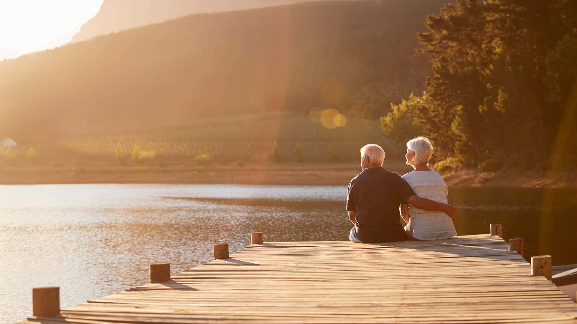 Widowed dating symbolized by a man and woman sitting next to each other on a dock end enjoy the sundowner
