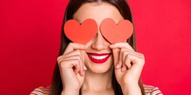 Young girl smiling holding hearts over her eyes