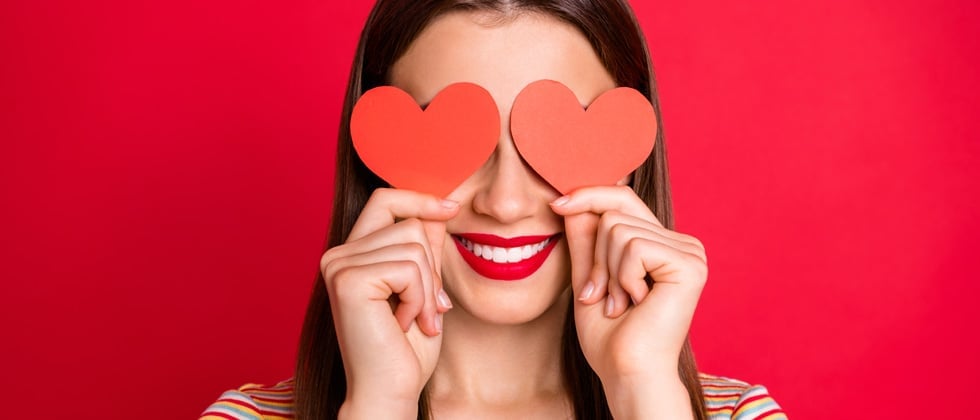 Young girl smiling holding hearts over her eyes