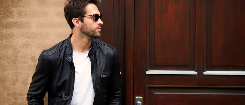 A guy in a leather jacket and sunglasses looking away as he walks