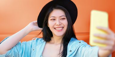 A dark-haired young woman wearing a black hat poses for a selfie