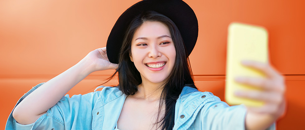 A dark-haired young woman wearing a black hat poses for a selfie