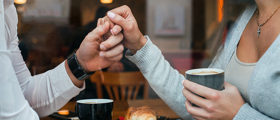 A couple hold hands over a table in a cafe