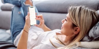 Woman laying on her couch casually while holding her phone