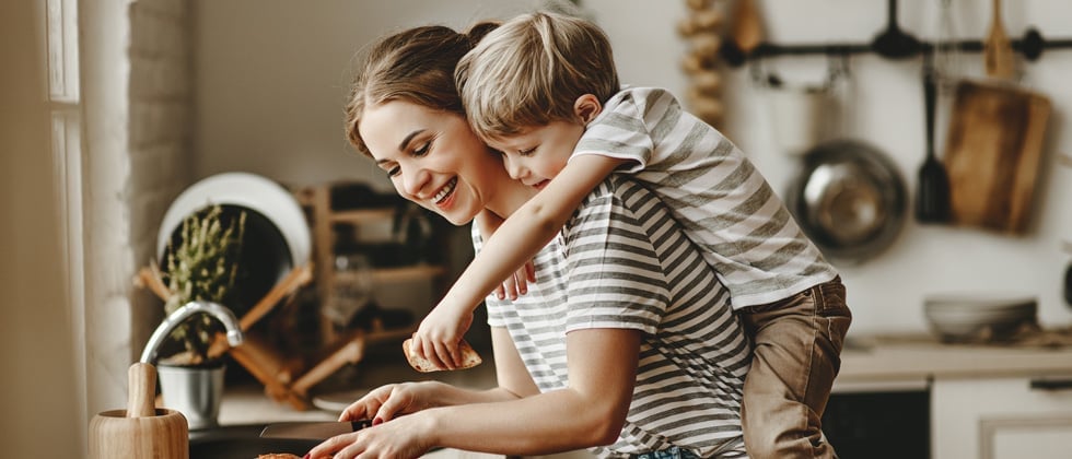 A mom cooking with her son on her back in the kitchen