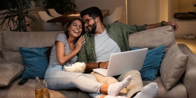 Woman and a men sitting on the sofa with popcorn watching a movie on the laptop and having date night at home