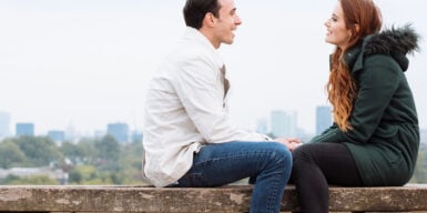 Man and woman sitting on bench looking at each other as symbol for first date tips