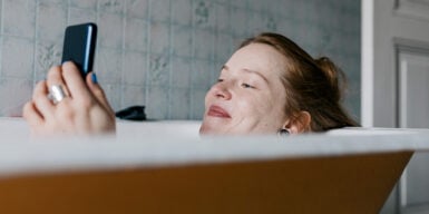 Woman sitting in bathtub with cell phone as example for questions to ask a guy