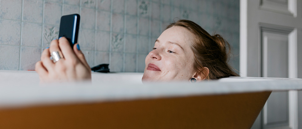 Woman sitting in bathtub with cell phone as example for questions to ask a guy