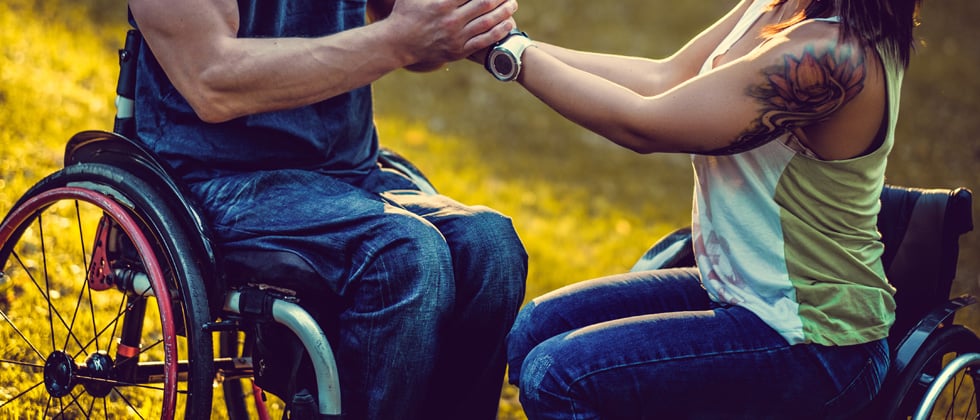 A couple in each in wheelchairs holding each other's hands