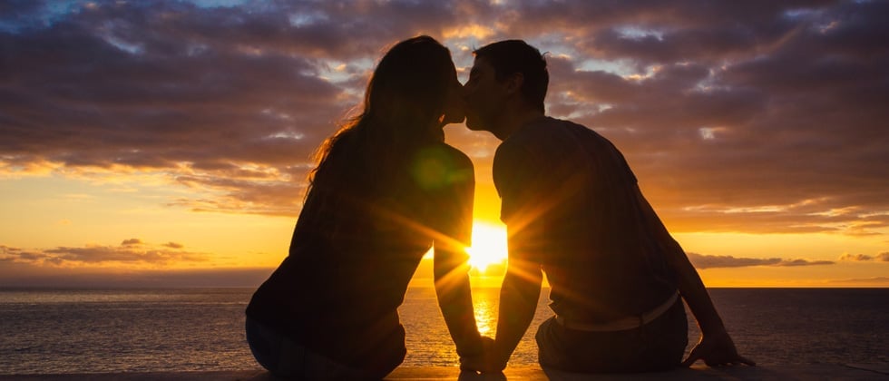 Couple kissing at sunset on the beach with the sun between them