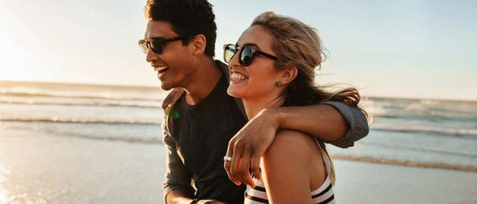Man and woman laughing together on the beach as a symbol of healthy relationship characteristics